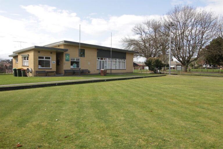 The Trafalgar Park Community Hub building seen from across the green, with trees and open sky behind