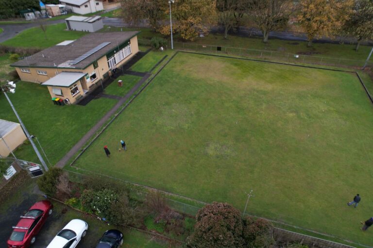 The green at the Hub seen from above, mown and edged, with the hall alongside