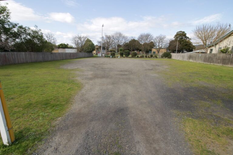 The Hub's gravel carpark, a wide flat open area running alongside the green behind a timber fence