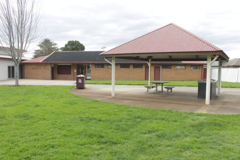 A roofed shelter with picnic tables and a barbecue on a paved area beside the Hub