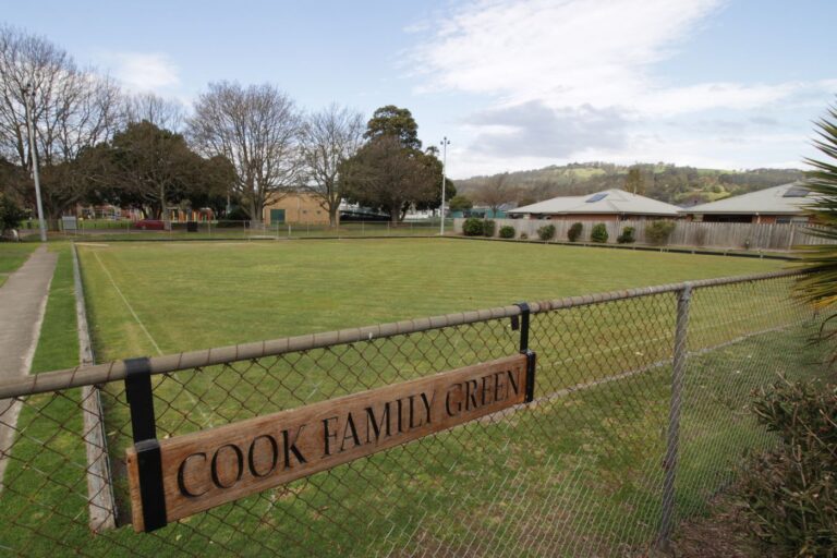 A timber sign fixed to the fence at the Hub reading 'Cook Family Green', with the green and the Gippsland hills behind