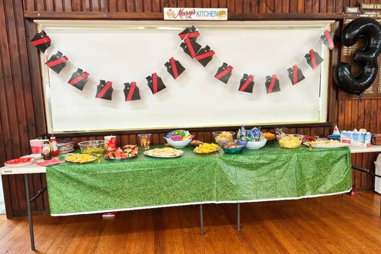 Party food laid out on a green tablecloth under the kitchen servery, with bunting and a number 3 balloon