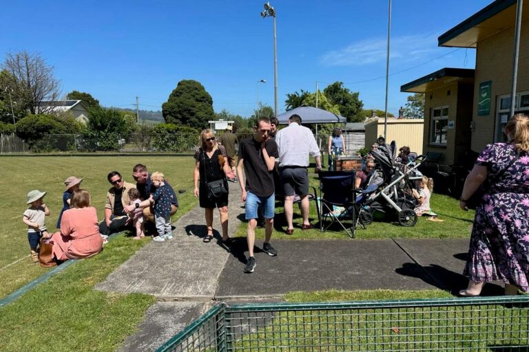 Families with prams and small children gathered on the grass beside the Hub building on a sunny day