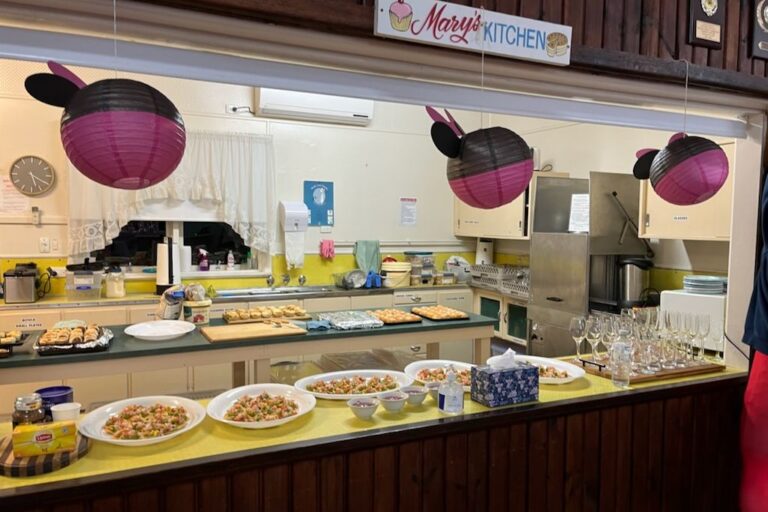 Plates of food and rows of glasses set out along the kitchen servery for a function