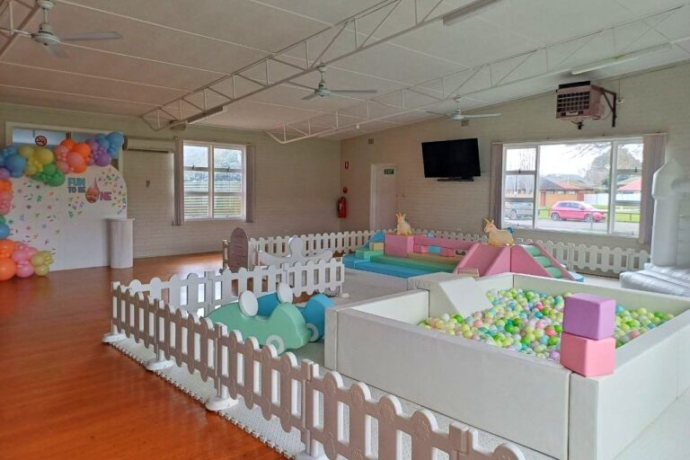 The hall set up for a children's party, with a fenced soft-play area and a ball pit